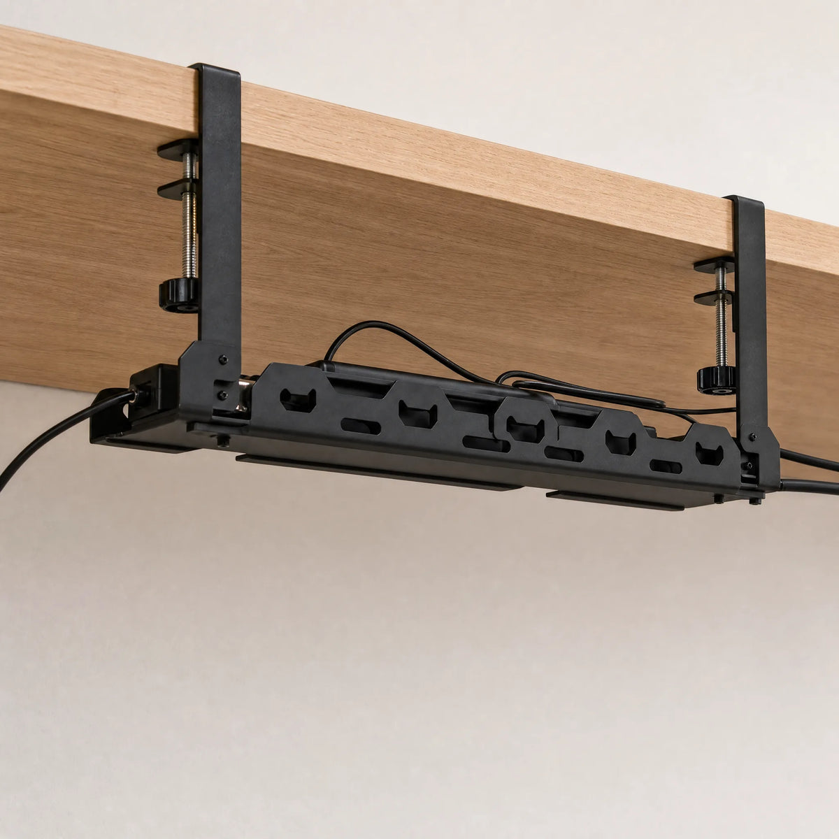 The cable tray clamped under a desk, holding a power strip and routed cables