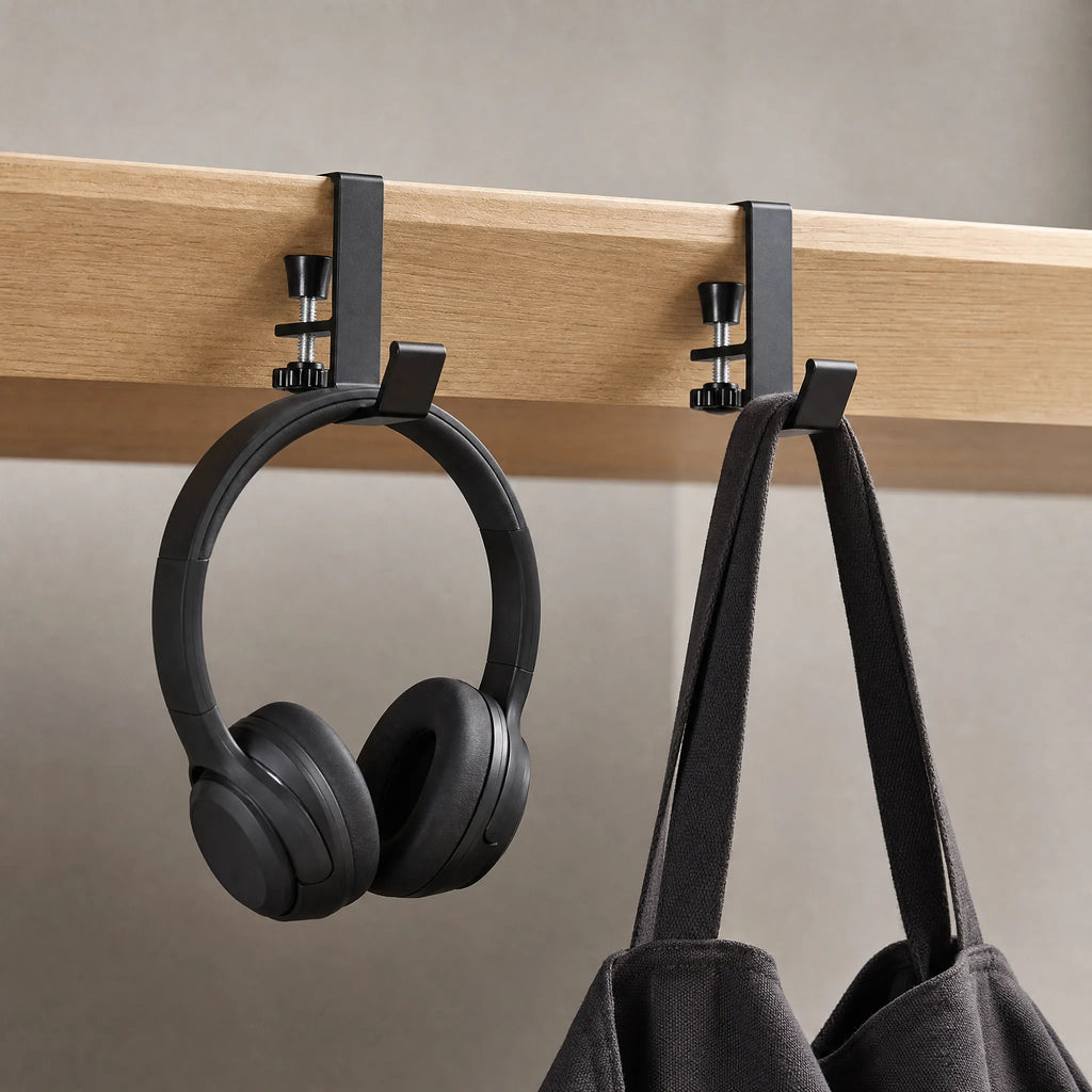Two edge hooks clamped to a desk edge, carrying headphones and a canvas bag